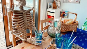 Une pièce décorée sur le thème du squelette, une table en bois avec des boissons, et une vue sur la mer par la fenêtre.