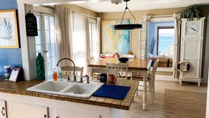 Une cuisine équipée d’un évier, un coin repas avec une table et des chaises, une horloge et une vue sur la mer.