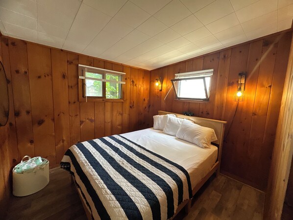 A wooden-paneled bedroom with a bed, two windows, and wall-mounted lights. - 2 Bdrm Cozy Cottage #1 close to town docks Lake Winnipesaukee - Meredith (Meredith)