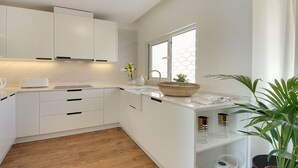 A modern kitchen with white cabinets, a wooden floor, a window with a hexagonal pattern, and a potted plant. - Boavista Apartment - Vintage & romantic! (Albufeira)