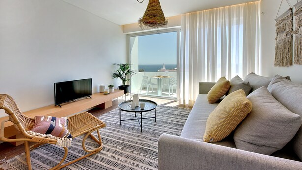A modern living room with a sofa, a wicker chair, a small round table, and a television. - Boavista Apartment - Vintage & romantic! (Albufeira)