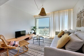 Ein modernes Wohnzimmer mit einer Couch, einem Korbsessel, einem kleinen runden Tisch und einem Fernseher.