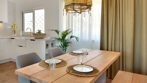 A dining area with a wooden table set for four, a wicker basket, and a potted plant. - Boavista Apartment - Vintage & romantic! (Albufeira)
