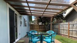Une terrasse avec une plateforme en bois, une table et des chaises, et un espace abrité doté d’un toit en métal.