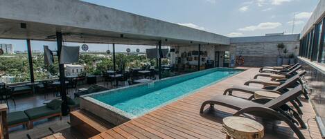 Un área de piscina en la azotea con sillones de descanso, un jacuzzi y vistas a la ciudad.