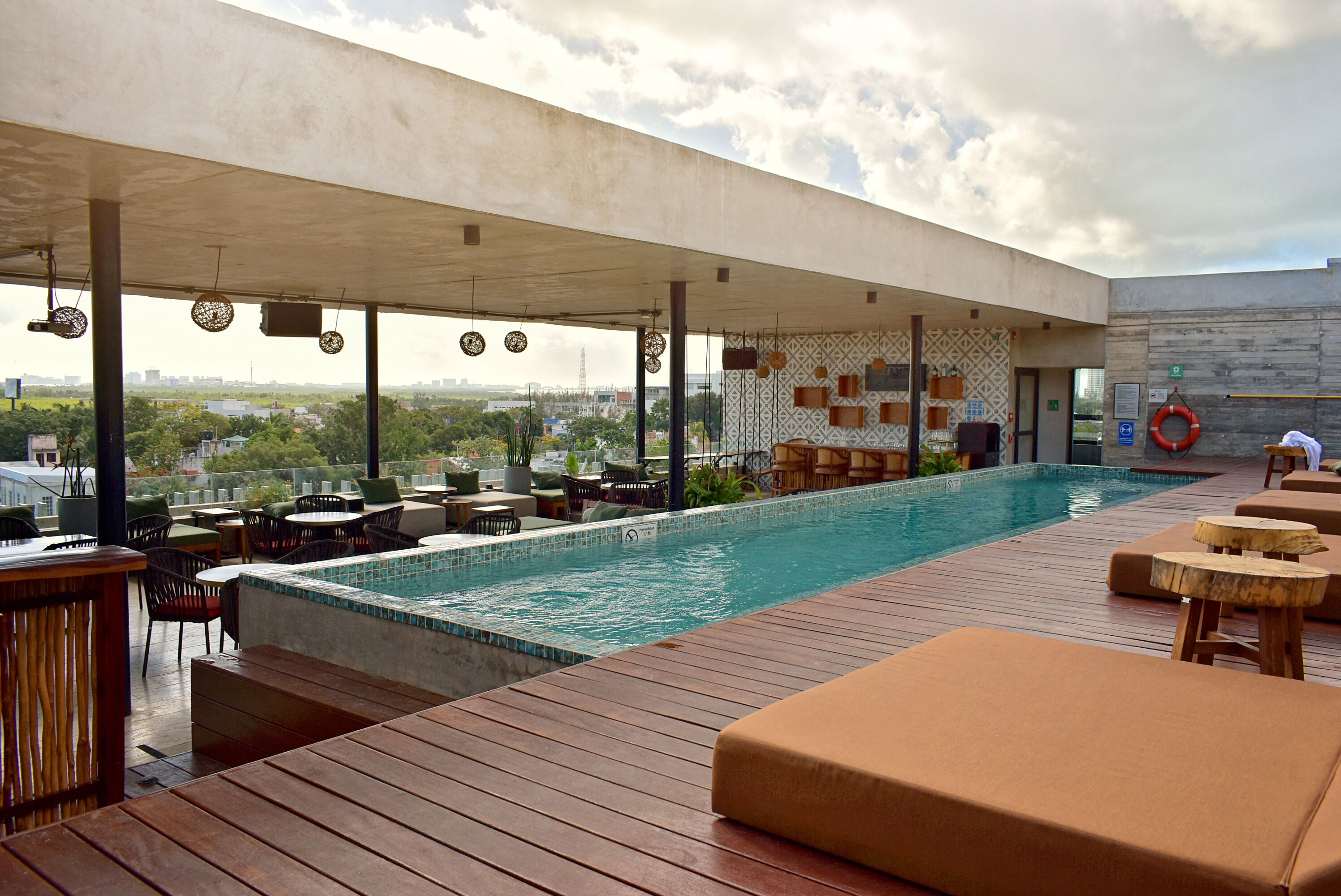 Zona de piscina en la azotea con terraza de madera, sillas de descanso y vistas a la ciudad.