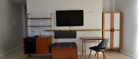 Habitació compacta amb televisió de pantalla plana penjada a la paret, una taula de fusta petita, una banca amb coixins i una cadira.