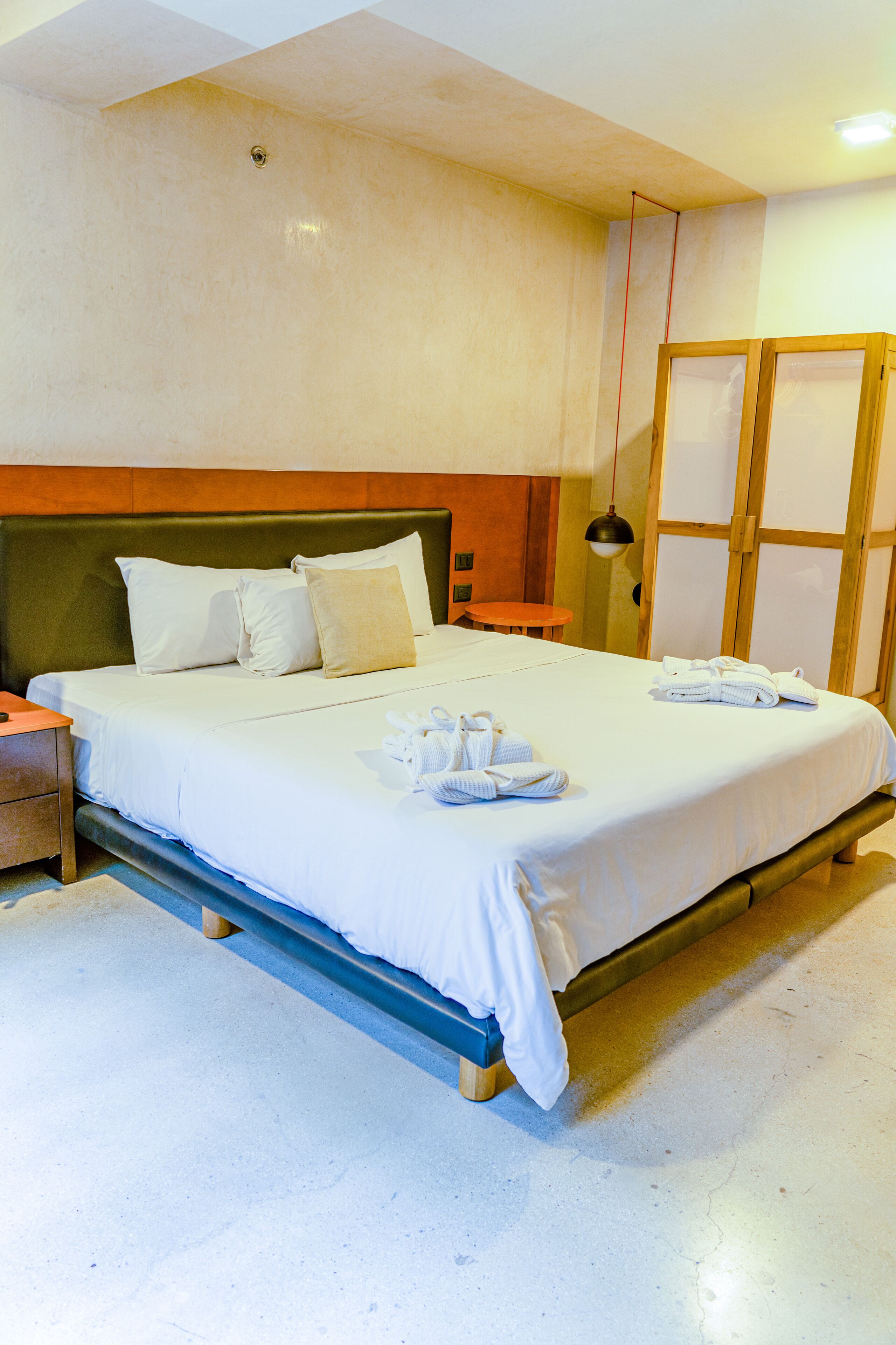 A neatly made bed with white linens and towels, a wooden headboard, and a small table beside the bed.