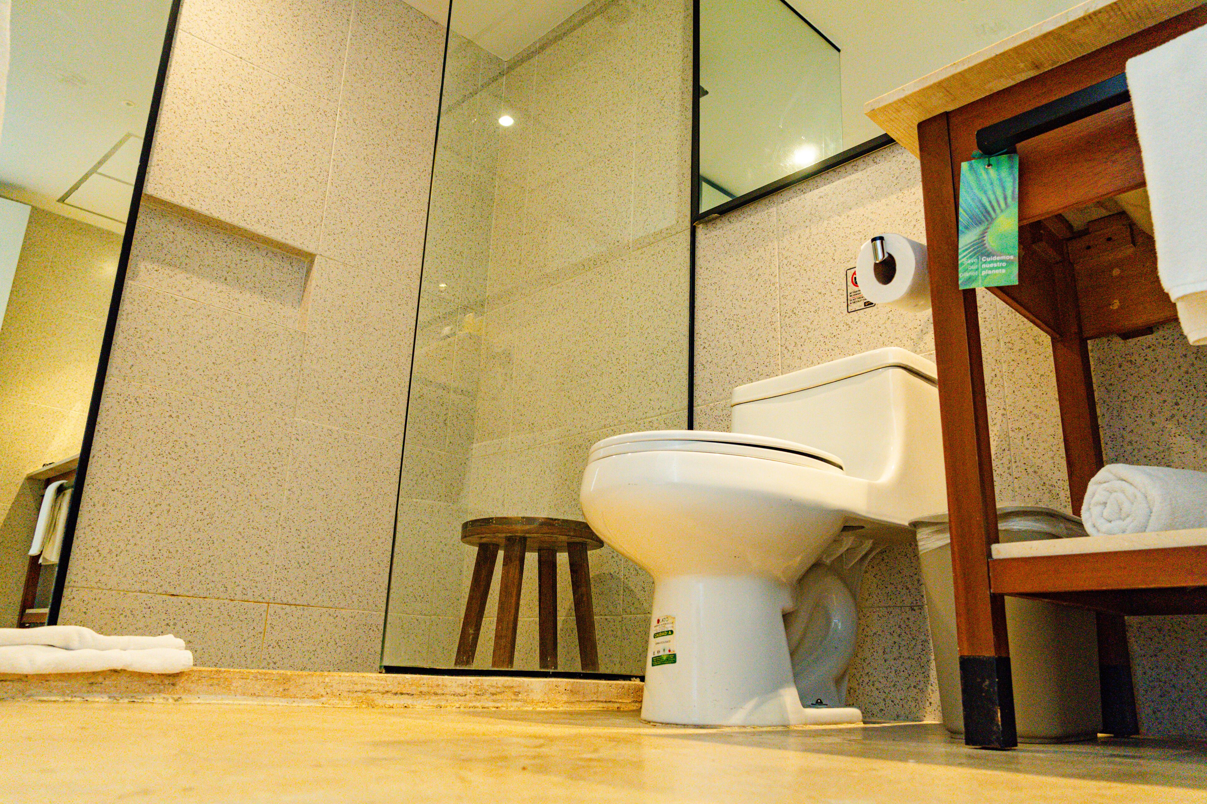 Un baño con inodoro, un taburete de madera, una toalla y una cabina de ducha de vidrio.