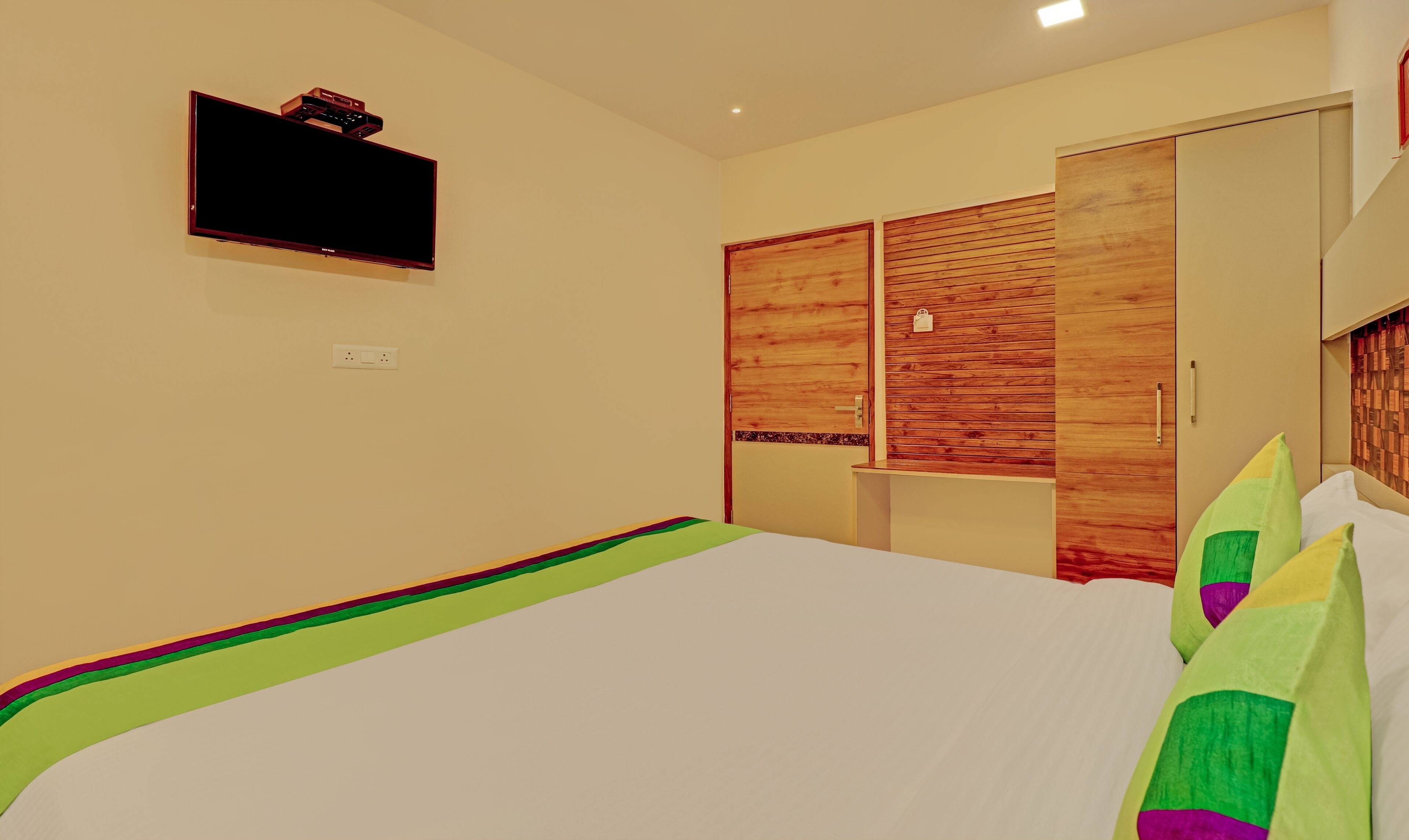 Un dormitorio con cama, televisión instalada en la pared y armarios de madera.