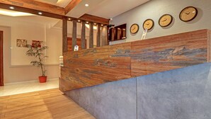 Zona de recepción con mostrador de madera, una planta en maceta y un reloj de pared.