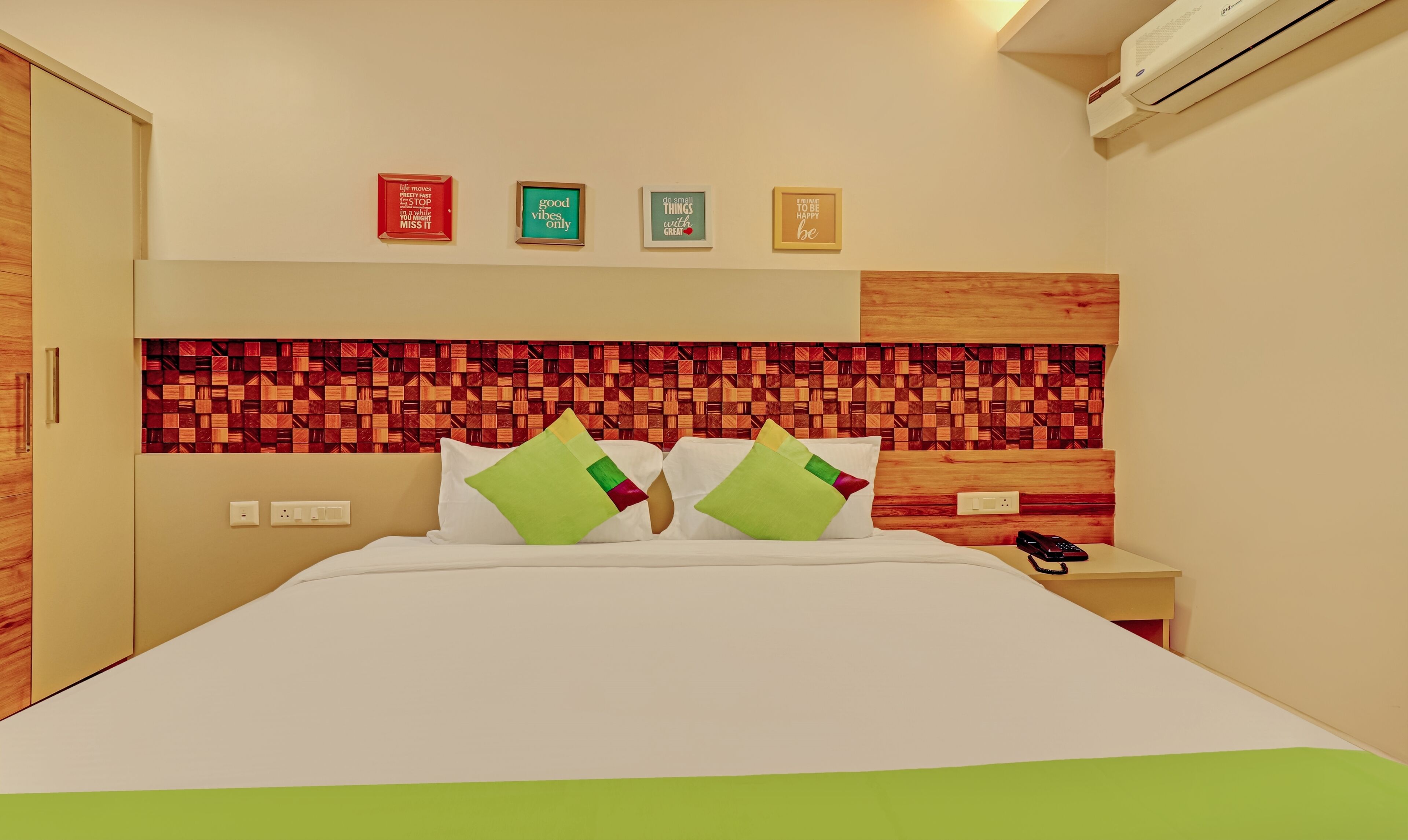 A hotel room with a bed, two bedside tables, a nightstand, and a wall with four framed motivational quotes.