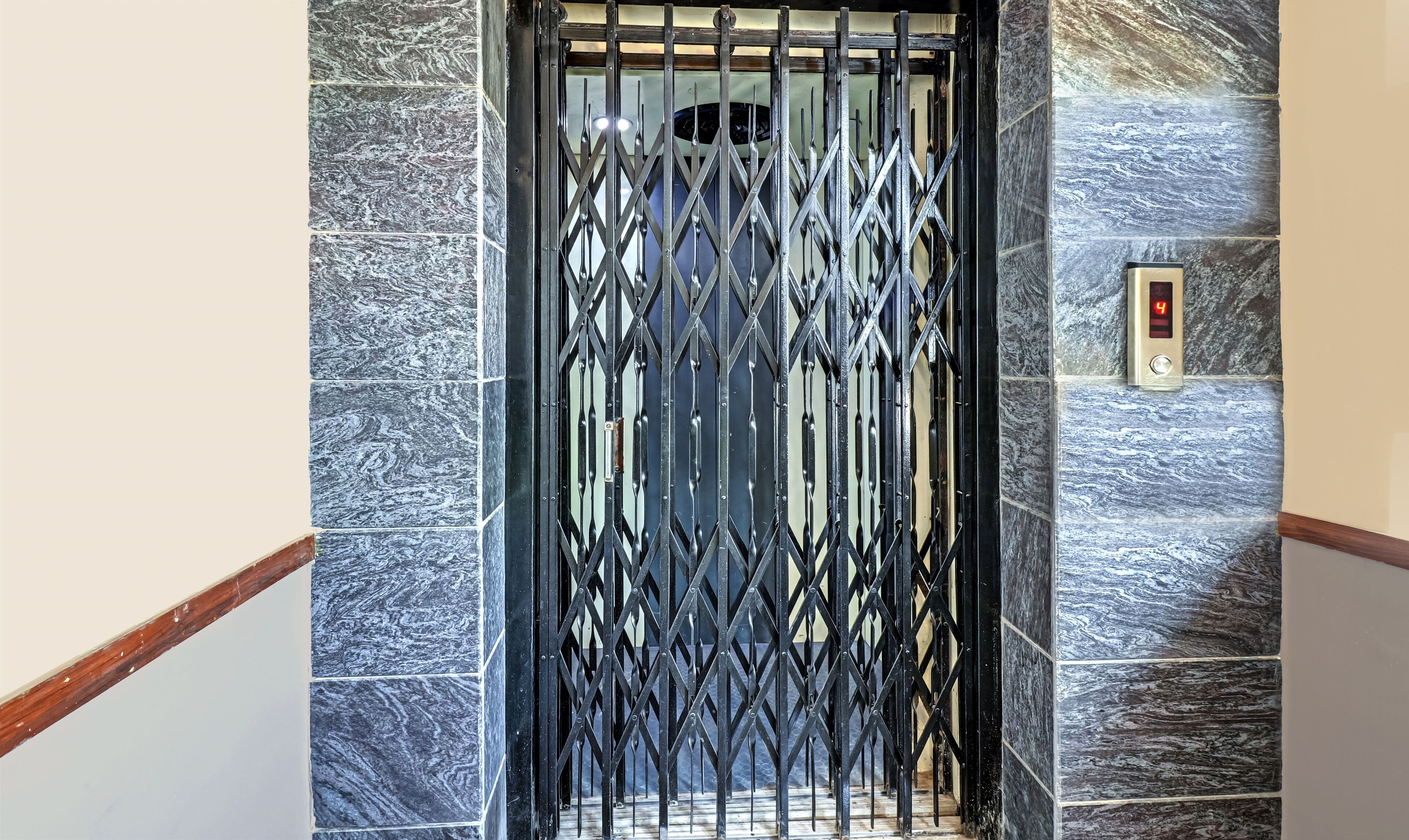 An elevator with a metal grille door, marble walls, and a digital display showing the number 4.