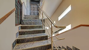 Una escalera con escalones de mármol y barandillas de metal, que conduce a un rellano con vistas al exterior.