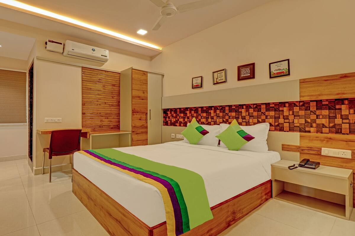 A modern hotel room with a wooden headboard, a bed with colorful pillows, a desk, and a chair.