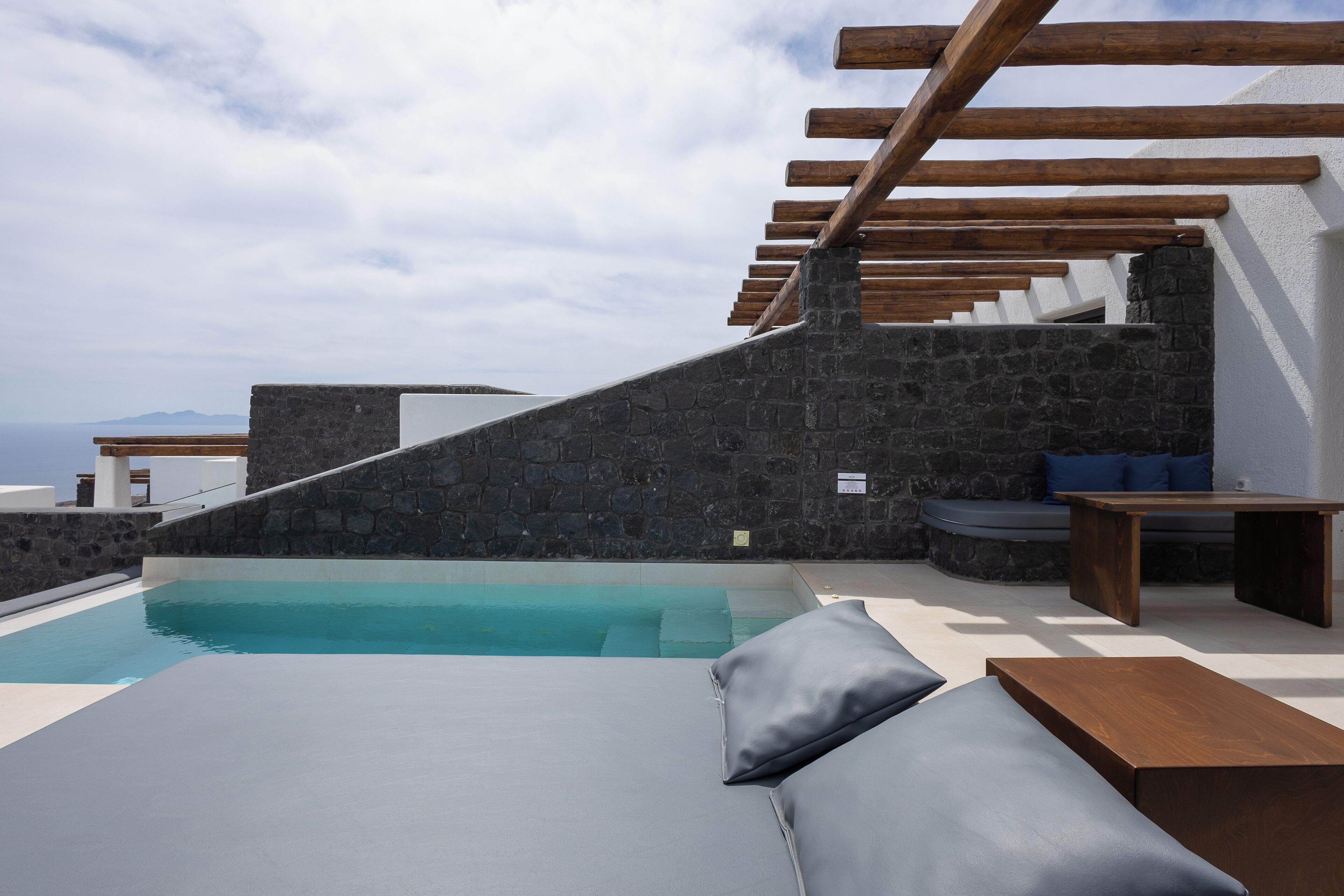 A modern outdoor pool area with stone walls, wooden pergola, and seating.