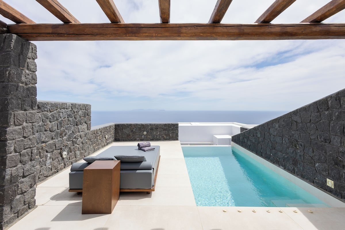 Un espace piscine aménagé sur le toit, avec des murs en pierre, une pergola en bois et une vue sur la mer.