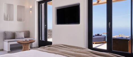 A bedroom with a large bed, a wooden bench, a small table, a TV, and a balcony with a view.