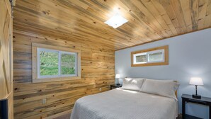 Een slaapkamer met een houten plafond, twee ramen, een bed en bedlampjes.