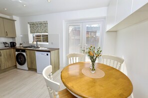 A modern kitchen with a washing machine, dishwasher, and a dining area with a wooden table and chairs. - A house that sleeps 4 guests  in 2 bedrooms (Cromer)