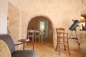 Une pièce aux murs de pierre, équipée d’un télescope, d’une table à manger avec des chaises et d’une petite table sur laquelle sont posés des livres.