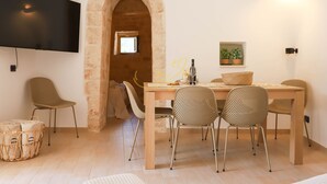 Un coin repas avec une table en bois, des chaises en osier et un téléviseur fixé au mur.