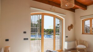 Une chambre d’hôtel avec un lit, une fenêtre donnant sur une piscine, un fauteuil en osier et un radiateur.