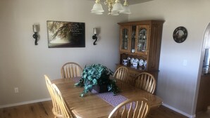 A dining room with a wooden table, six chairs, a potted plant, a wall-mounted light fixture, a decorative plate, and a cabinet with glass doors. - Country house in Montrose (Montrose)