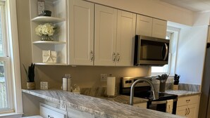 Una cocina moderna con armarios blancos, encimera de mármol y tres taburetes blancos.