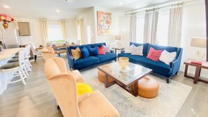 A modern living room with a blue sofa set, a beige armchair, and a glass coffee table.