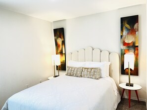 Een hotelkamer met een bed, twee bedlampen, een hoofdbord en twee abstracte schilderijen aan de muur.