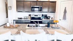A modern kitchen with granite countertops, stainless steel appliances, and a dining area with white chairs.