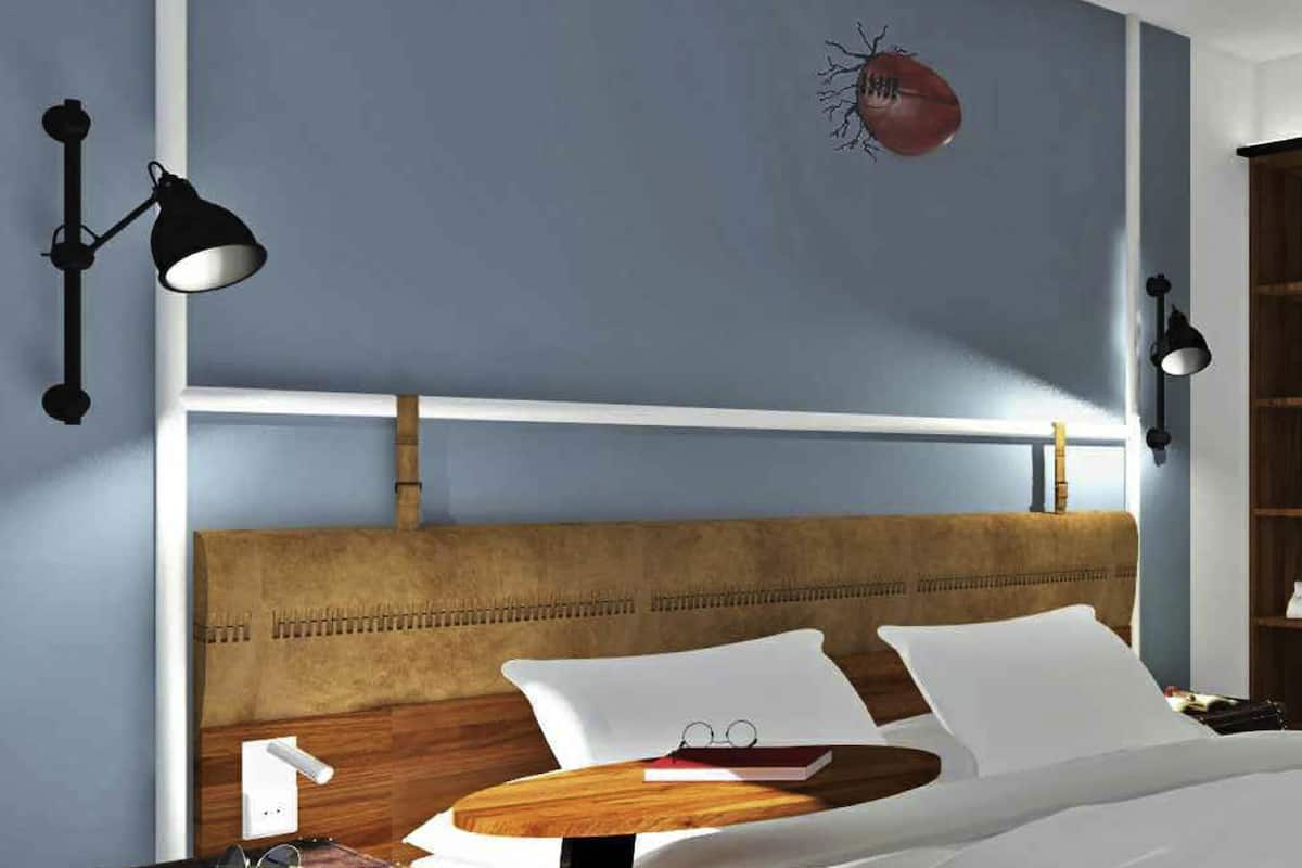 A bedroom with a wooden headboard, a bedside table with a book and glasses, and wall-mounted lamps.