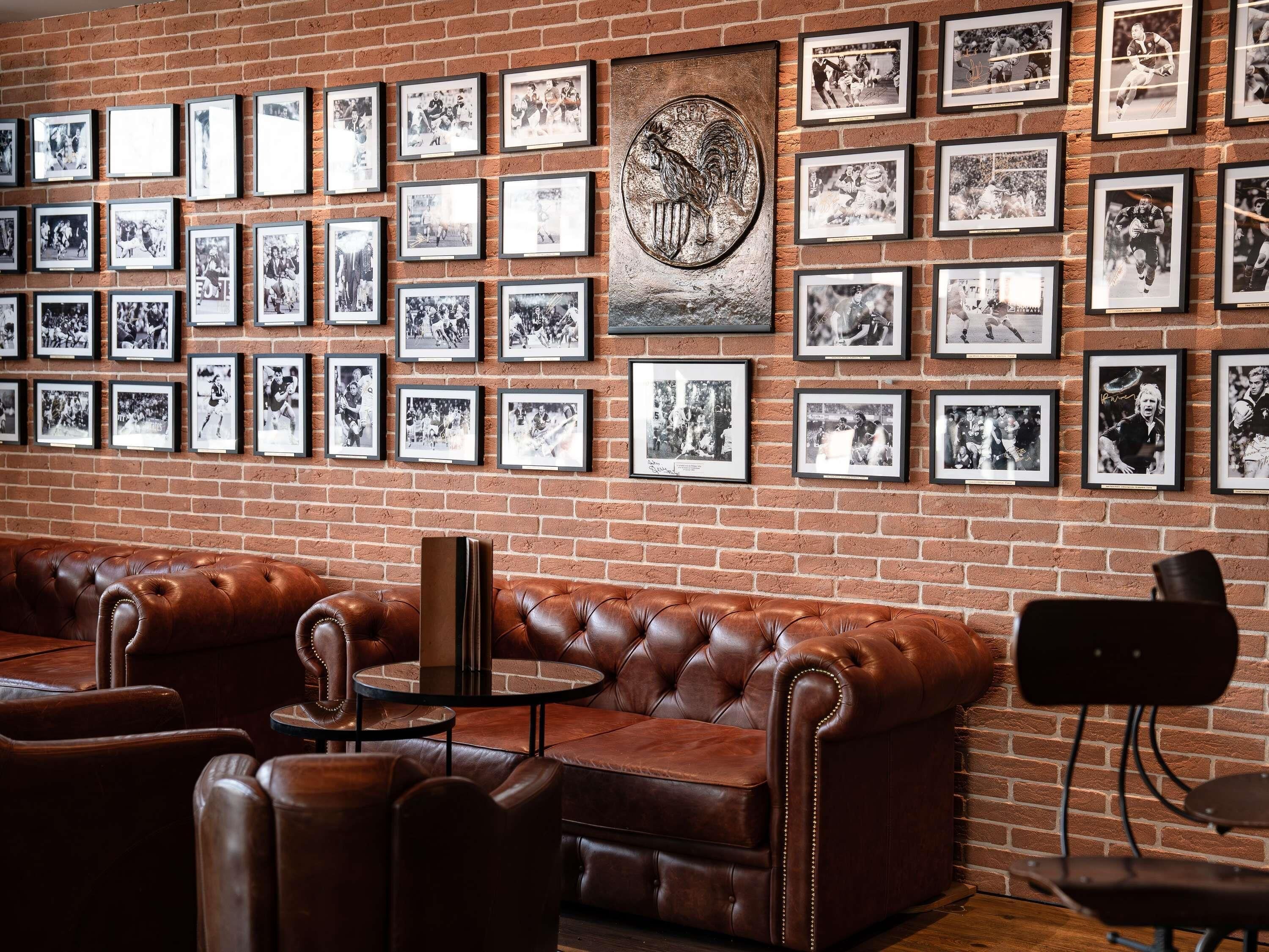 A brick wall with framed black and white photographs, a leather couch, and a round table.