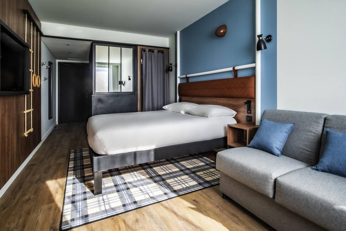 A modern bedroom with a bed, a sofa, a wooden floor, and a plaid rug.