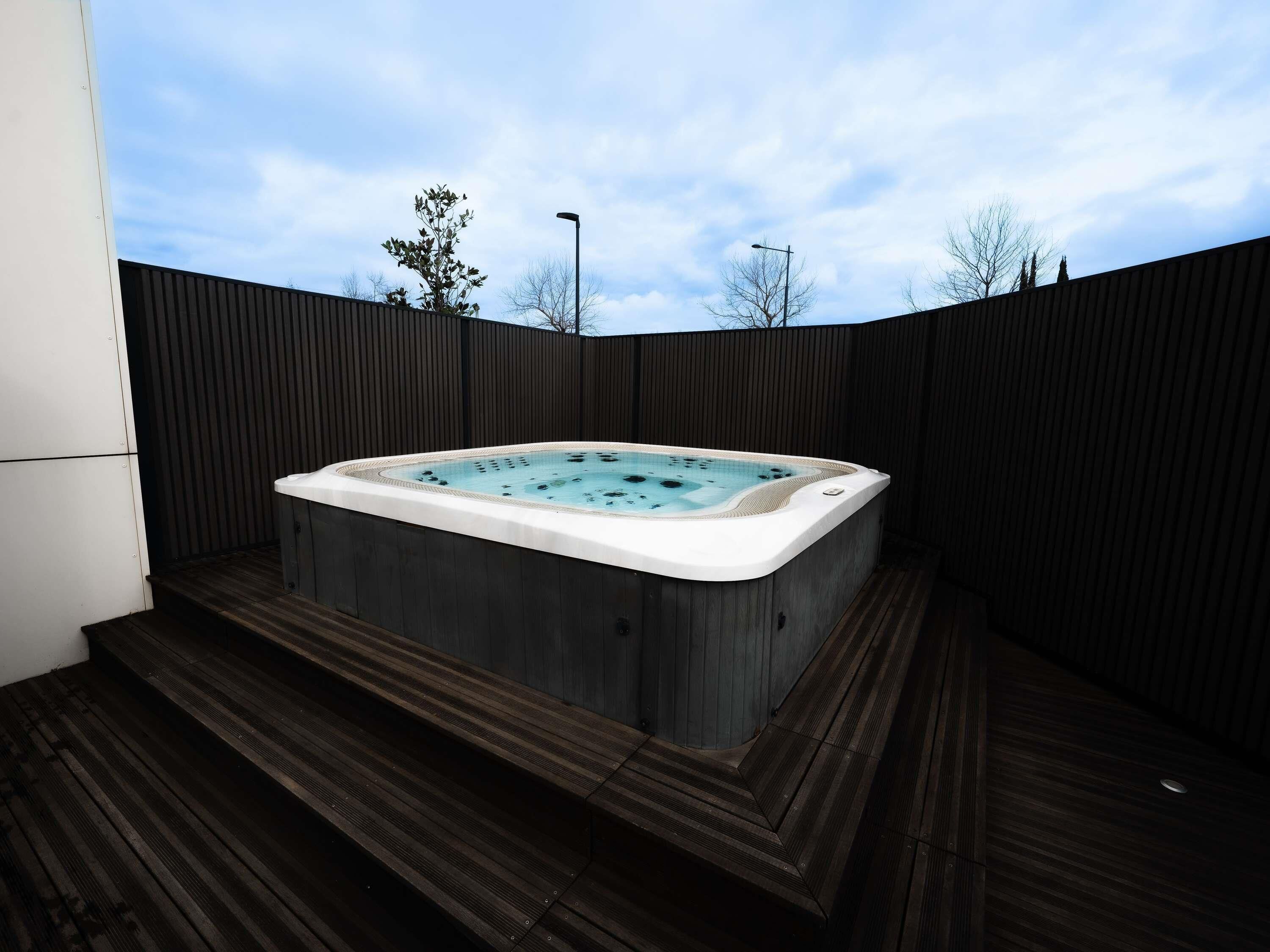 Un jacuzzi en un área de terraza de madera, con valla de madera y cielo despejado.