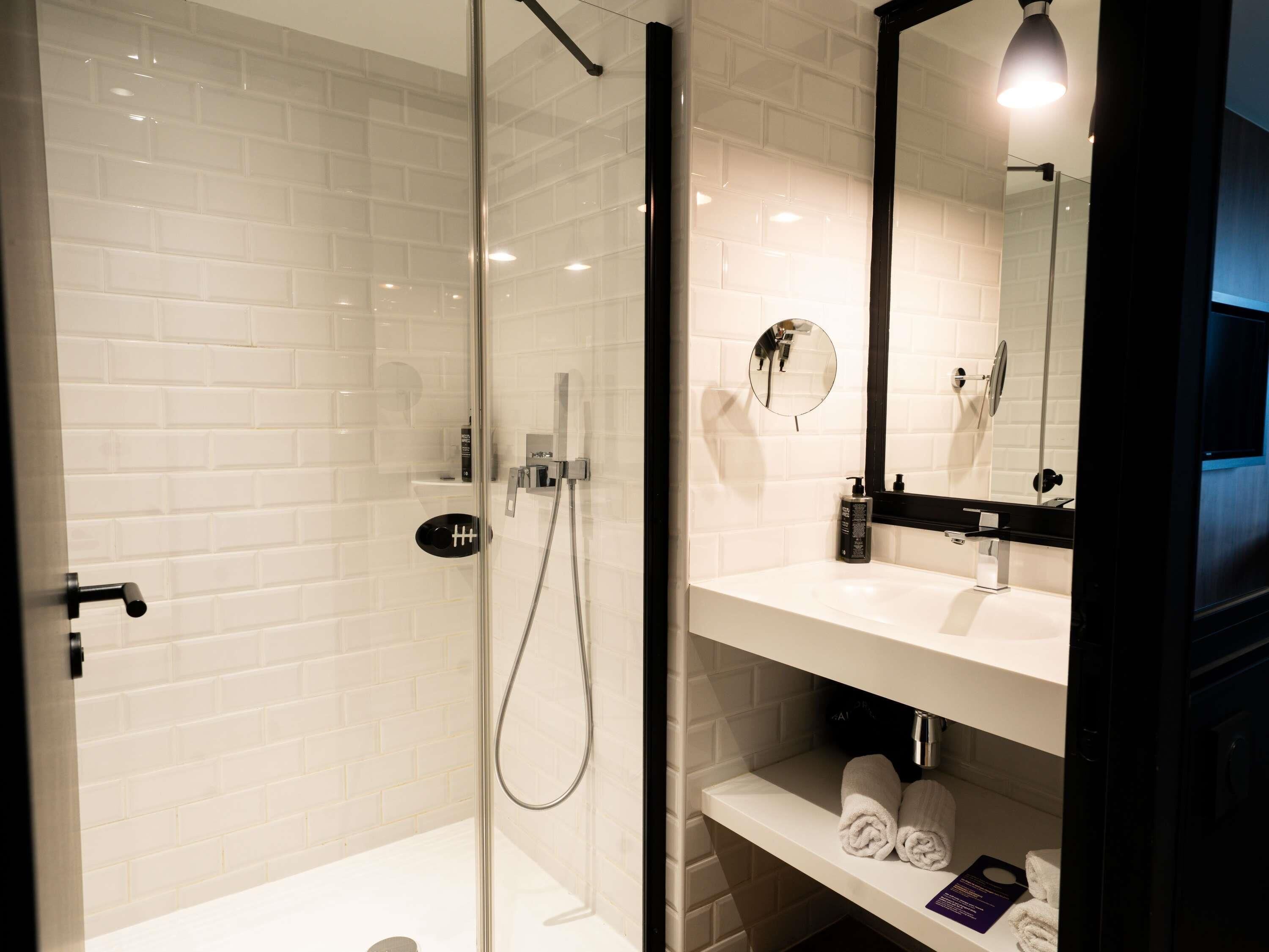 A modern bathroom with a glass-enclosed shower, white subway tiles, a black-framed mirror, and a white sink with a towel rack.