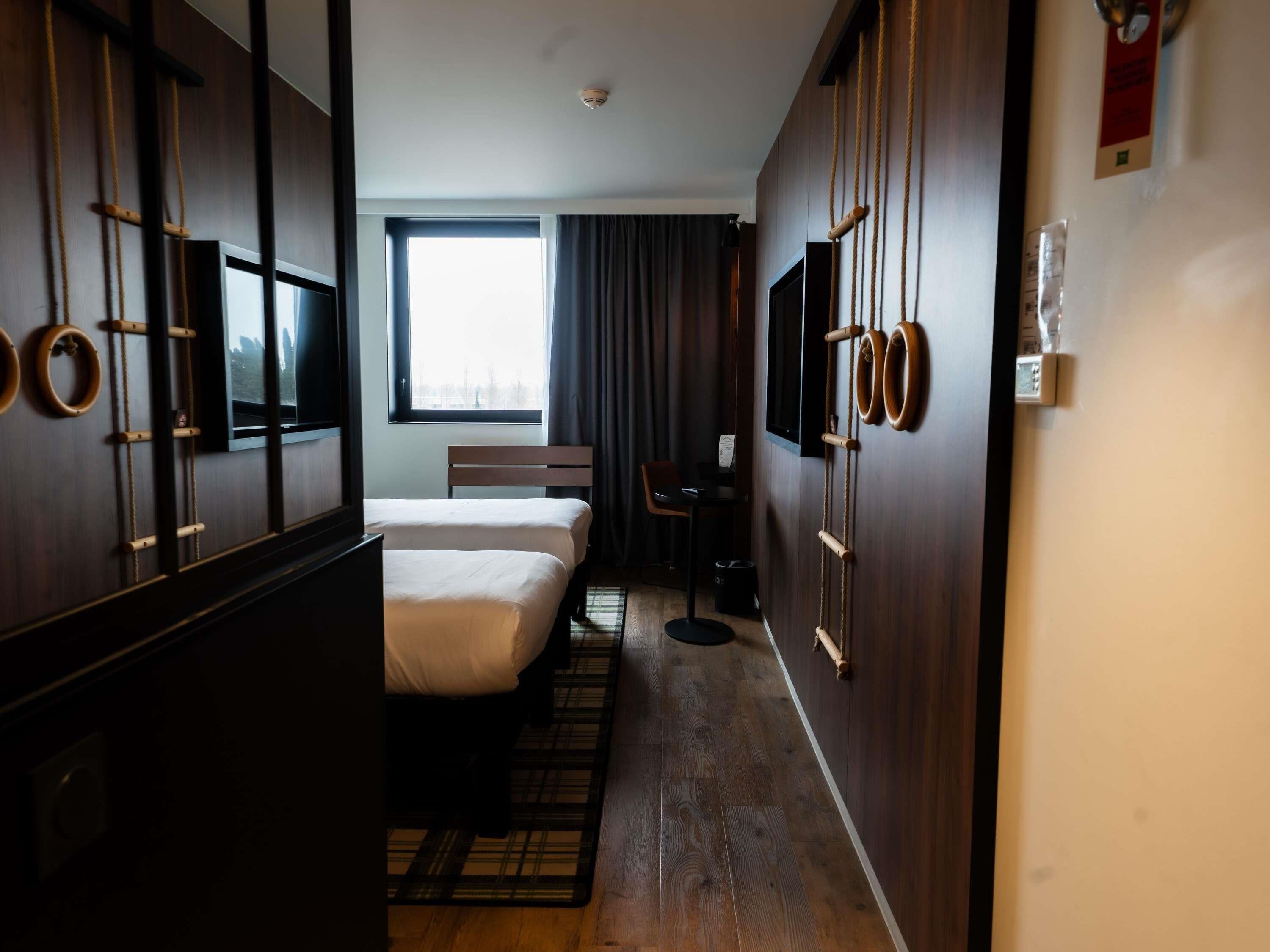 Hotellihuone, jossa on sänky, työpöytä, tuoli, televisio ja ikkuna, jossa on verhot.