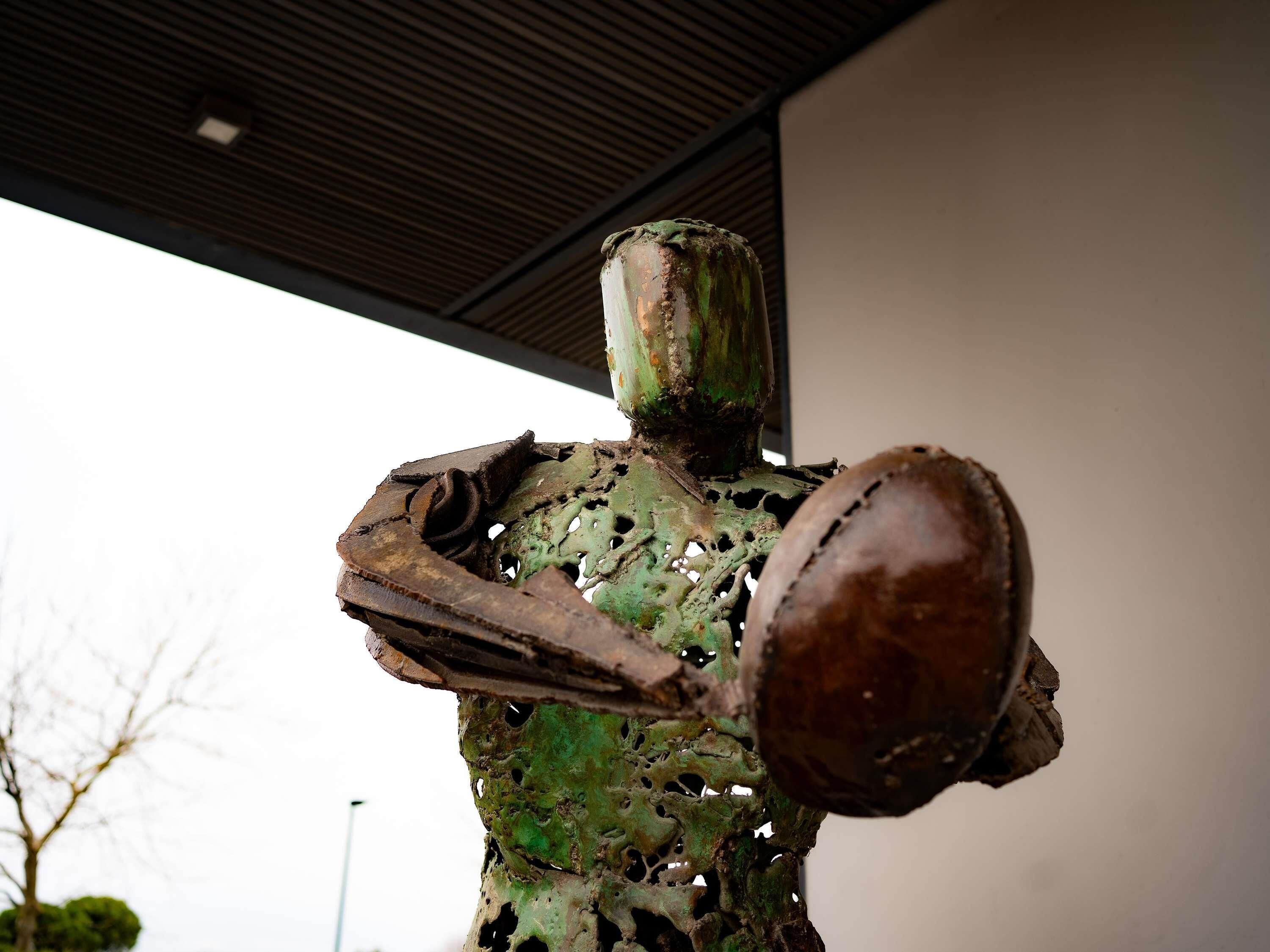 A sculpture with a greenish patina, rusted metal parts, and a cylindrical shape.