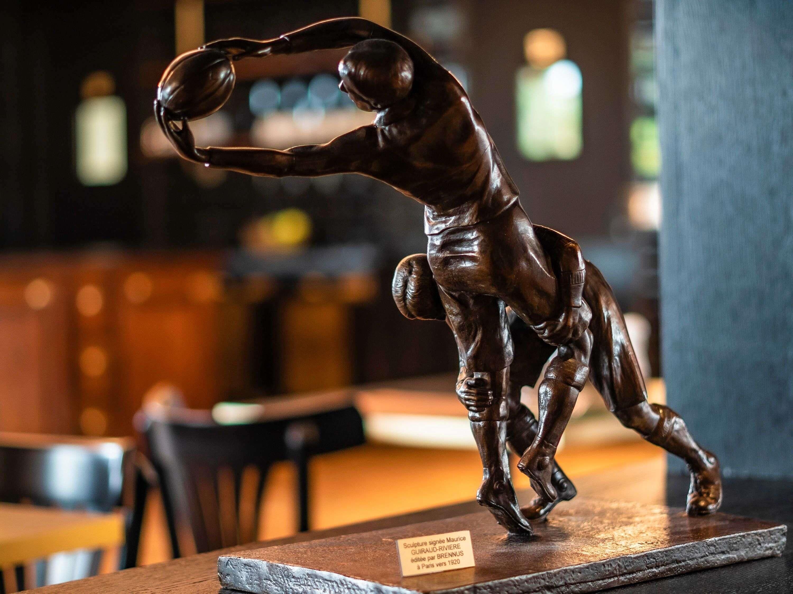 A bronze sculpture of a basketball player in motion, displayed on a wooden pedestal with a plaque.