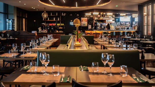 A restaurant with a central bar, multiple dining tables, and a modern ceiling design. - ibis Styles Castelnaudary (Castelnaudary)