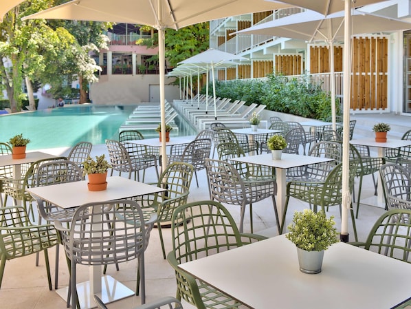 Espace extérieur aménagé avec des tables et des chaises, une piscine et un bâtiment avec une clôture en bois en arrière-plan.