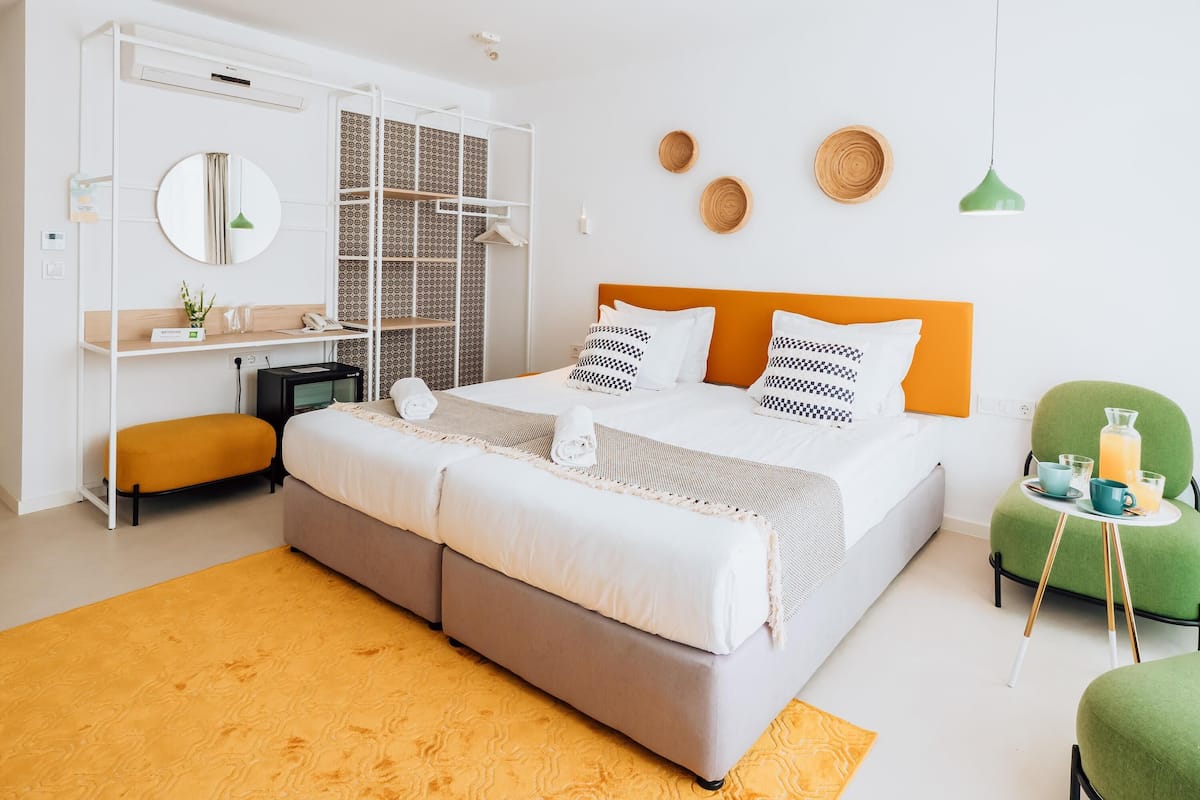 A modern hotel room with a bed, a desk, a chair, and a small table with a green chair.