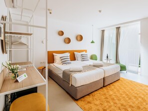 Une chambre d’hôtel moderne équipée d’un lit double, d’un bureau avec un ordinateur, d’une chaise, d’une petite table agrémentée d’un vase de fleurs et d’un balcon avec vue.