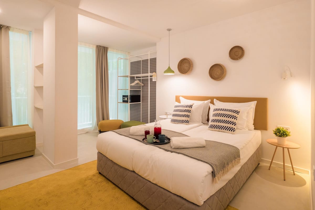 A modern hotel room with a large bed, a small table with a plant, and a seating area with a chair.