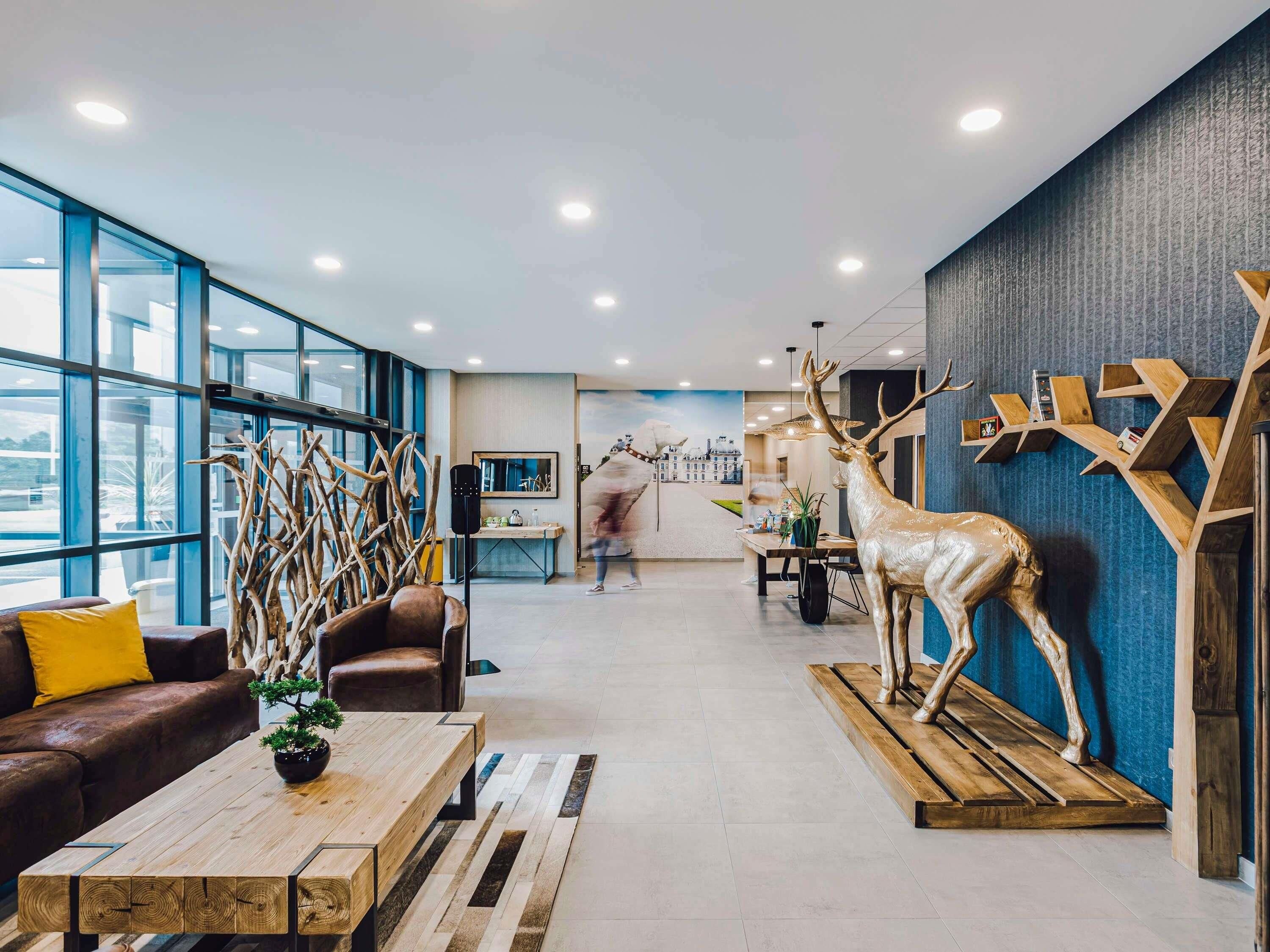 A modern interior with a large glass window, a wooden coffee table, a brown leather sofa, and a deer sculpture.