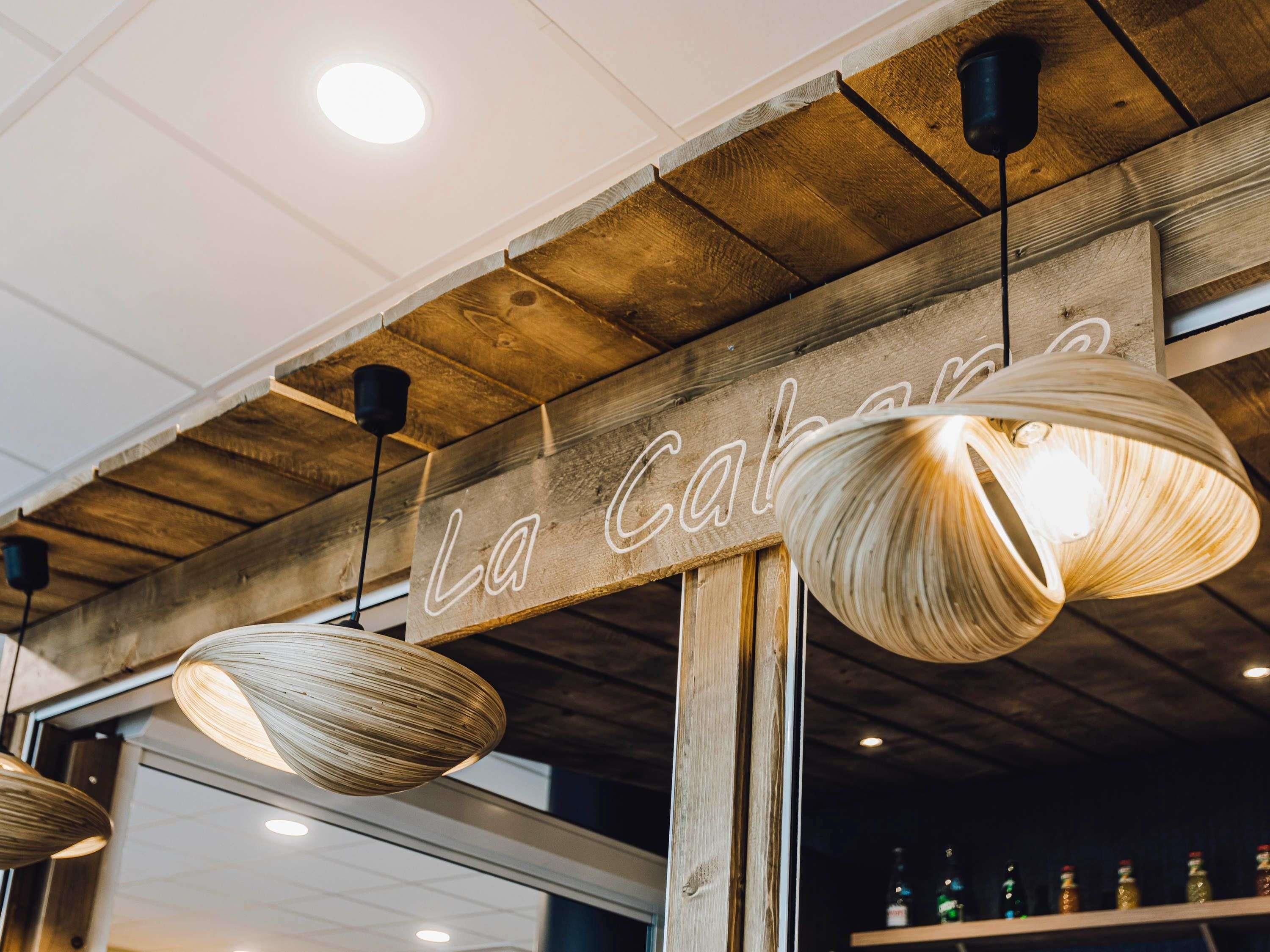 A wooden ceiling with a sign reading "La Cabaña" and hanging woven light fixtures.