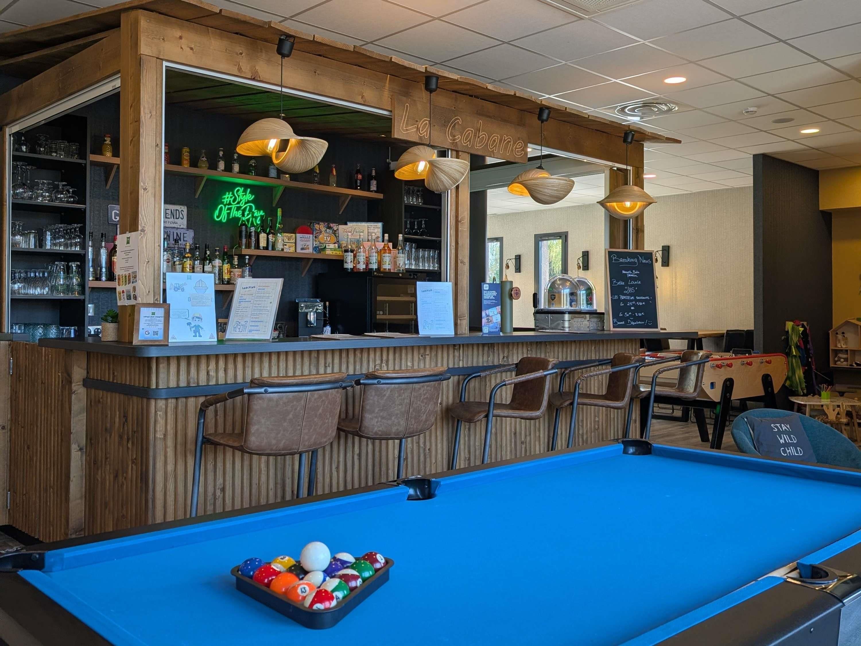 A pool table with balls, a bar area with shelves of bottles, and a neon sign.