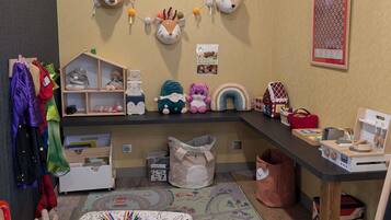 Een kinderspeelruimte met een plank, speelgoed, een vloerkleed en een wanddecoratie.