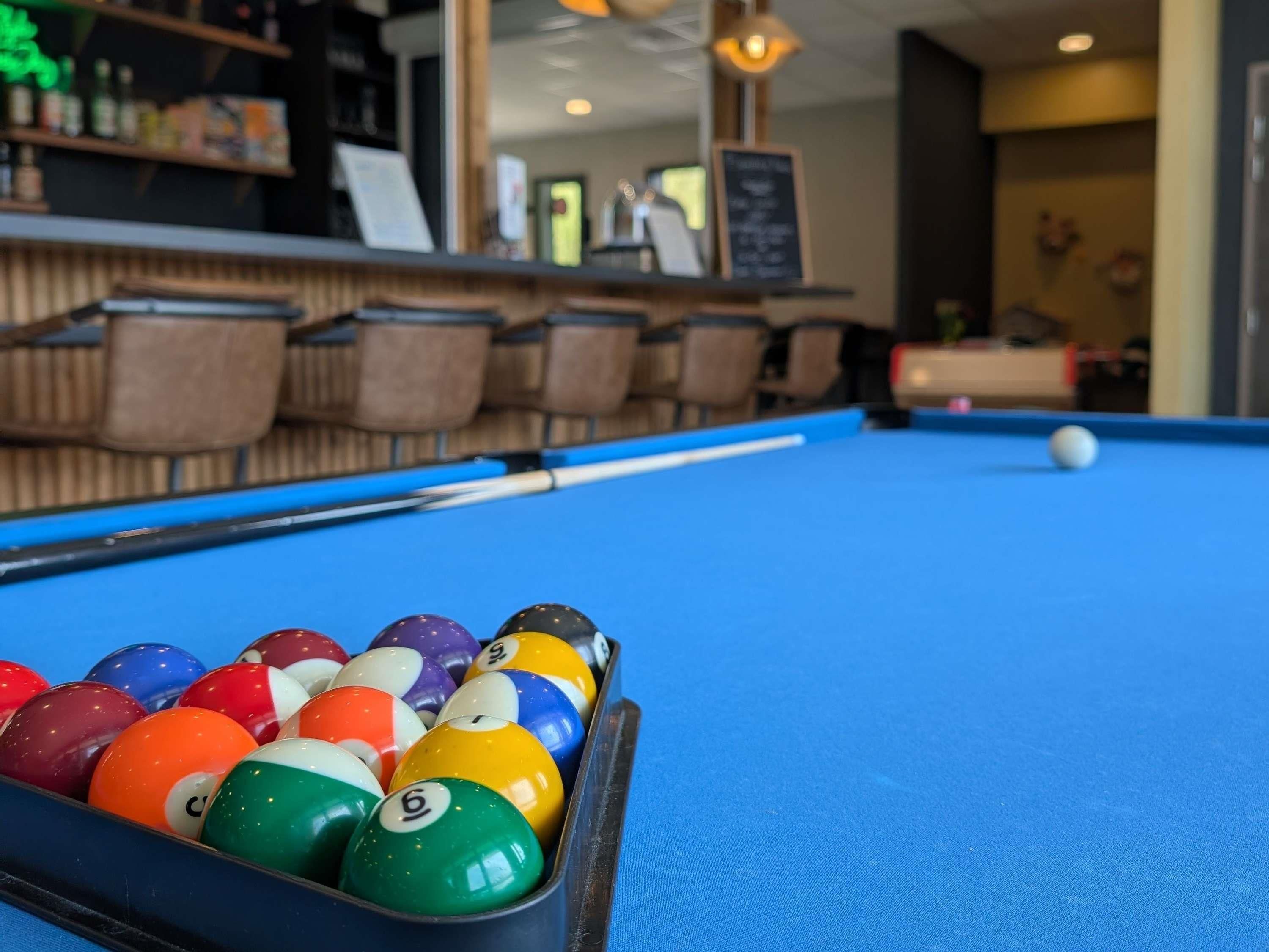 A pool table with balls, a bar area, and seating in a room.